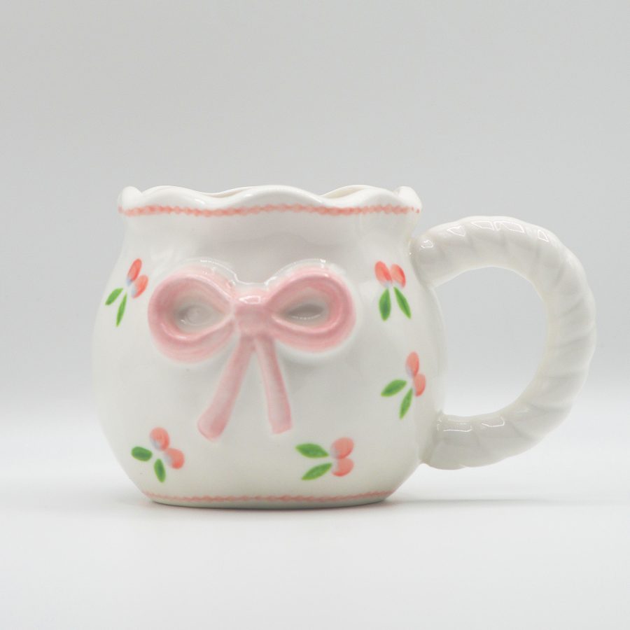 White ceramic mug with embossed pink bow and hand-painted floral accents